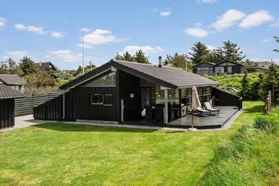 a black house with a deck in a yard at BL1203-Blokhus-Pirupshvarrevej-23 in Blokhus