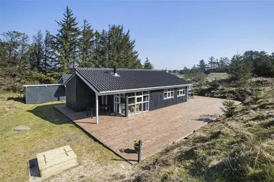 a small black house on a hill with a deck at BL180-Blokhus-Soren-Petersvej-22 in Blokhus