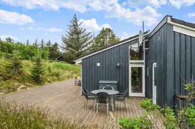 a black house with a table and chairs on a deck at BL180-Blokhus-Soren-Petersvej-22 in Blokhus