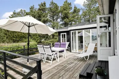 a deck with a table and chairs and an umbrella at BL1556-Blokhus-Poppelvej-1 in Blokhus