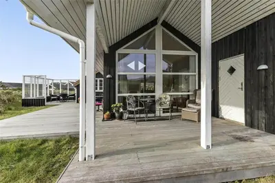 a house with a wooden deck with a large window at BL964-Blokhus-Klitvejen-28 in Blokhus