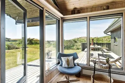 a room with large windows and a blue chair on a porch at BL1755-Saltum-Karen-Mariesvej-57 in Saltum