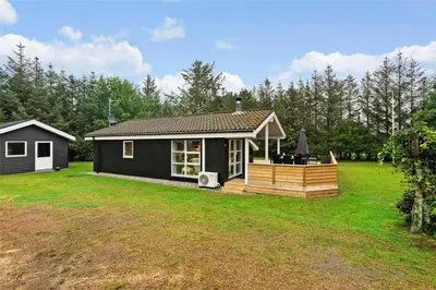 a small black house with a deck on a yard at BL762-Blokhus-Berberisvej-49 in Blokhus