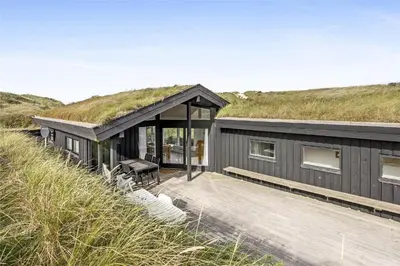 a black house with a grass roof with a deck at BL358-Pandrup-Kaskelotten-5 in Pandrup