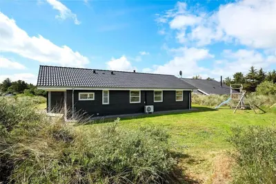 a black house in a field with a yard at BL417-Blokhus-Saetergaardsstien-6-A in Blokhus
