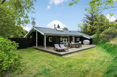 a black cottage with a deck and chairs on it at BL1627-Blokhus-Lyngvej-17 in Blokhus