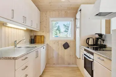 a small kitchen with white cabinets and a window at BL1304-Blokhus-Bag-Hojen-45 in Blokhus