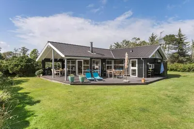 a house with a deck and chairs in the yard at BL935-Blokhus-Tobaksvej-1 in Blokhus