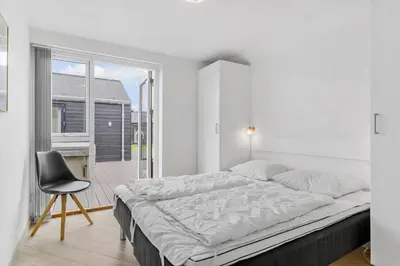 a white bedroom with a large bed and a chair at BL234-Blokhus-Sdr-Strandvej-9-A in Blokhus