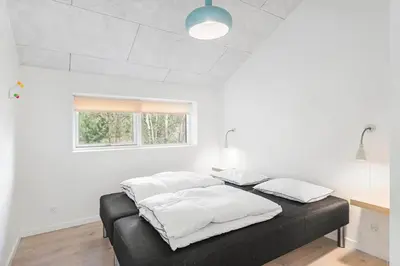 a bedroom with a bed with white sheets and a window at BL1367-Blokhus-Saetergaardsstien-12 in Blokhus