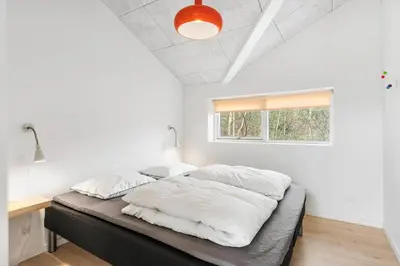 a bedroom with a bed with white sheets and a window at BL1367-Blokhus-Saetergaardsstien-12 in Blokhus