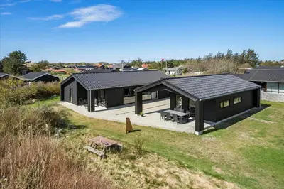 a house with a black roof on a field at BL1651-Blokhus-Pirupshvarrevej-21 in Blokhus