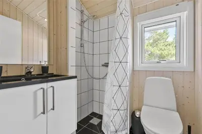 a bathroom with a toilet and a sink and a window at BL1139-Blokhus-Sletten-3 in Blokhus