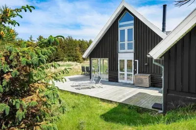 a black house with a wooden deck in the grass at BL1362-Saltum-Kronhjortvej-19 in Saltum