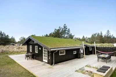 a black house with a grass roof with a deck at BL1330-Blokhus-Risen-3 in Blokhus