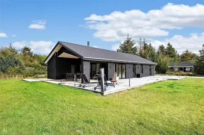 a small black house with a deck in a field at BL1442-Blokhus-Bag-Hojen-43 in Blokhus
