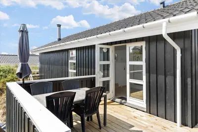 a black house with a deck with a table and chairs at BL362-Blokhus-Klitvejen-42 in Blokhus