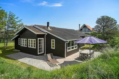 a small house with an umbrella and a patio at BL220-Blokhus-Bakkevaenget-9 in Blokhus