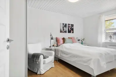 a white bedroom with a white bed and a chair at BL1206-Blokhus-Blaabaervej-6 in Blokhus