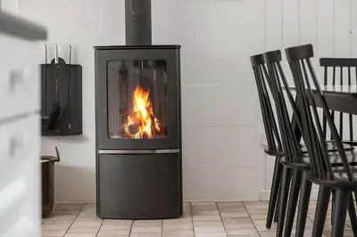 a stove with a fire in a room with chairs at BL253-Blokhus-Jaegerbakken-9 in Blokhus
