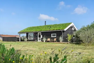 a black house with a grass roof with two chairs at BL806-Saltum-Laustvej-8 in Saltum