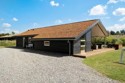 a black house with a roof on a gravel driveway at BL1762-Blokhus-Bloksbjerg-22 in Blokhus
