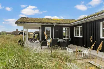 a black house with a deck with a table and chairs at BL1564-Blokhus-Ved-Skoven-8 in Blokhus