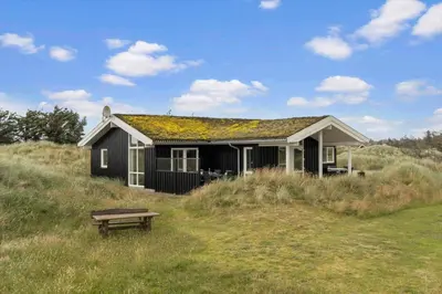 a small black house with a bench in a field at BL1564-Blokhus-Ved-Skoven-8 in Blokhus