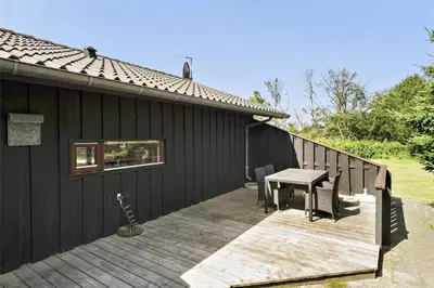 a wooden deck with a table and a house at BL236-Blokhus-Pirupshvarrevej-27 in Blokhus