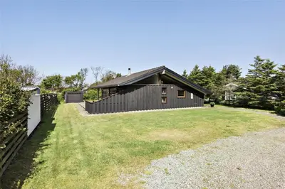 a house with a fence in front of a yard at BL236-Blokhus-Pirupshvarrevej-27 in Blokhus