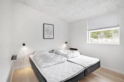 a white bedroom with a bed and a window at BL1134-Blokhus-Bloksbjerg-17-B in Blokhus