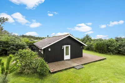 a black shed with a deck in a yard at BL1218-Blokhus-Quintusvej-24 in Blokhus