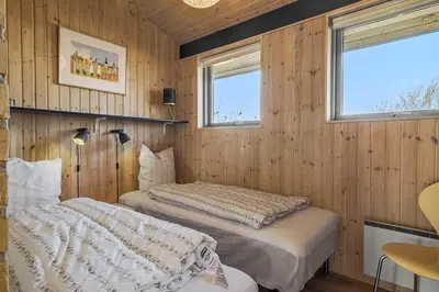 two beds in a room with wooden walls and windows at BL1232-Blokhus-Pirupvejen-91 in Blokhus