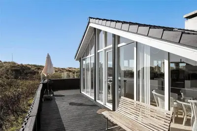a house with a deck with a table and an umbrella at BL971-Blokhus-Slugten-10 in Blokhus