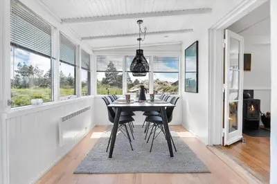 a dining room with a table and chairs and windows at BL1550-Blokhus-Poppelvej-10 in Blokhus