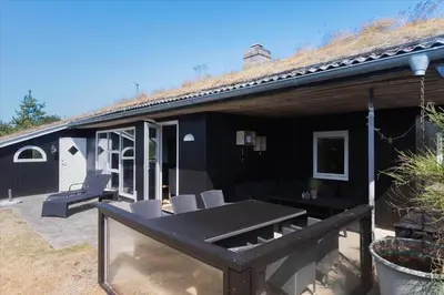 a black house with a table and chairs on a patio at BL1136-Blokhus-Graevlingevej-6 in Blokhus