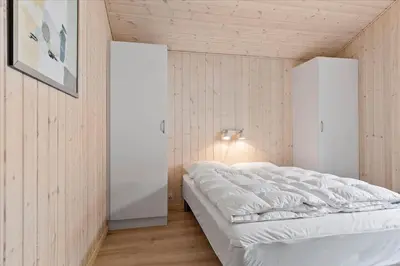 a bedroom with a white bed in a room with wooden walls at BL239-Blokhus-Klitgaardsvej-21 in Blokhus