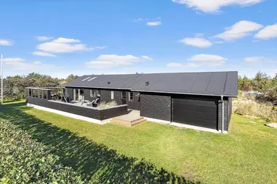 a house with a black roof on a grass field at BL1317-Blokhus-Frederiksensvej-5 in Blokhus