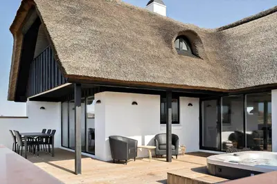 a thatch roofed patio with chairs and a table at 258-Harboore-Merchantvej-5 in Harboør