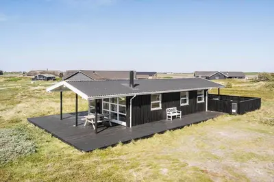 a black house with a deck in a field at 311-Harboore-Lille-Flyvholmvej-10-a in Harboør
