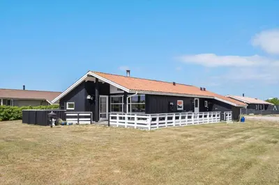 a black house with a white fence in a yard at 111-Harboore-Vejlby-Klit-125 in Harboør