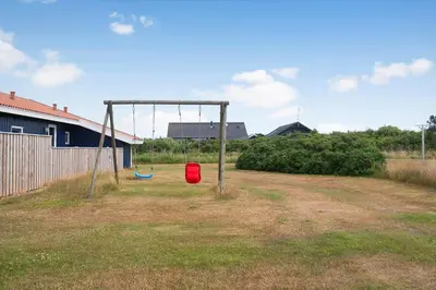 a swing set in a field with a red bucket at 138-Harboore-Neerlandiavej-6 in Harboør