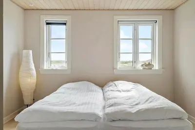 a bed with white sheets in a room with two windows at 187-Harboore-Neerlandiavej-1 in Harboør