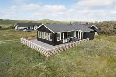 a black house with a deck in a field at 355-Harboore-Gloryvej-14 in Harboør
