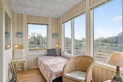 a bedroom with a bed and a chair and windows at 355-Harboore-Gloryvej-14 in Harboør