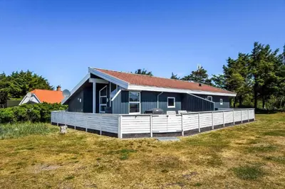 a blue house with a white fence in a field at 102-Harboore-Vejlby-Klit-21 in Harboør