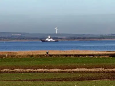 a boat on the water with a windmill in the distance at Scenic Retreat in Boddum - By Traum Ferienwohnungen in Boddum