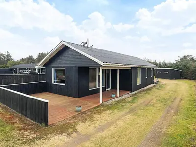 a black house with a deck in a field at 6 person holiday home in Løkken in Løkken