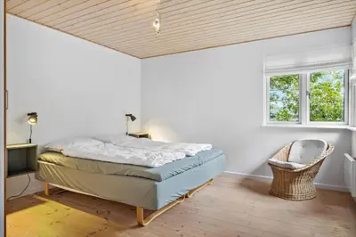 a bedroom with a bed and a chair and two windows at BL1107-Blokhus-Soren-Petersvej-16 in Blokhus