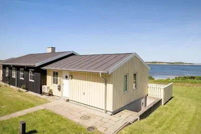 a small house with a black roof and the ocean at LF15112-Farso-Strandvejen-12-A in Farsø